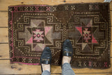 Distressed Oushak rug detail showing geometric pattern, dark chocolate, and bright pink.