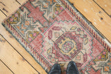 Worn blush and ivory Oushak rug mat texture with raspberry motifs, beneath black shoes.