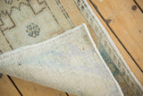 Folded corner of vintage distressed Oushak rug reveals worn pile and hand-knotted foundation.