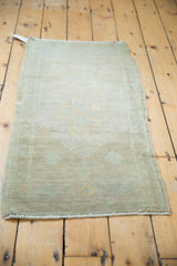 Distressed vintage Oushak rug end with low pile, pale seafoam vine border, and fringe.