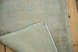 Folded distressed Oushak rug, showing low pile with pale seafoam design and woven foundation.