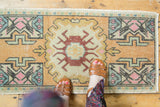 Distressed Oushak rug with central floral vase motif in muted sandalwood, terracotta, and pink.
