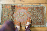 Feet on a distressed Oushak rug showing its pink medallion and worn terracotta, bronze field.