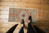 Distressed vintage Oushak rug corner featuring apricot, seafoam, fuchsia geometric motifs and visible pile wear.