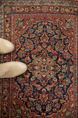 Navy blue field with cherry red, blush, and gold scrolling floral patterns on a vintage Kashan rug.