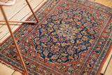 Vintage Kashan rug detail: threadbare cherry red border, navy floral patterns, tattered edge.