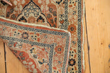 Folded corner of antique Haji Jalili Tabriz rug, intricate borders, dusty rust, navy, tattered edge.