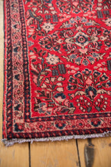 Corner of vintage American Sarouk rug, cherry red field, blush floral motifs, navy border, ivory fringe.