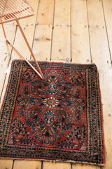 Hand-knotted Sarouk mat: brick red field, navy floral medallion, classic spandrel corner details.
