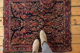 Vintage American Sarouk rug's dark navy ground, intricate floral motifs, and tattered edge.