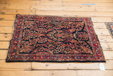 Vintage American Sarouk rug corner: intricate red floral bouquets on navy, with low pile and frayed end.