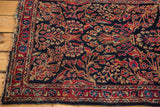 Vintage Sarouk rug corner: intricate red, beige florals on dark navy ground, tattered edge.