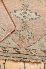Evenly worn peach and green Oushak rug with visible foundation, showing tattered fringe.