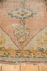 Worn pile texture of a vintage Oushak rug, showing faded peach apricot, rams horn finial, and tattered end.
