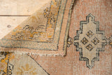 Vintage Oushak rug corner showing worn apricot pile, tattered sides, and hand-knotted reverse.