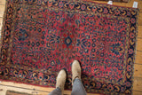 Vintage Persian Sarouk rug corner with dusty red floral field, color variations, and navy border.