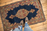 Scalloped Rococo medallion on vintage Kerman rug with indigo field, rose border, tattered edge.