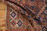 Folded vintage Caucasian rug displays navy, madder root red, and ivory geometric guls with texture.
