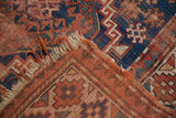 Vintage Caucasian rug corner folded, showing tattered fringe, madder red, and navy blue patterns.