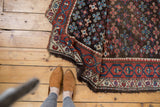 Kurdish antique rug displaying geometric medallions in madder red and teal with tattered ends.