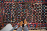 Madder red, teal blue geometric medallions on an antique Kurdish rug with visible wear.