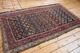 Antique Kurdish rug's geometric border in madder red, teal, ivory, with visible side tatter.