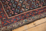 Antique Kurdish rug corner: madder red, teal blue geometric border, charcoal field, worn edge.