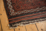 Tattered end of an antique Belouch rug, showing chestnut, charcoal, and ivory striped kilim.