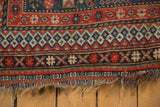 Vintage Qashqai rug end: brick red and navy geometric borders, exposed foundation.