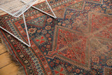 Vintage Qashqai carpet's intricate geometric patterns, brick red, navy blue, and visible wear.