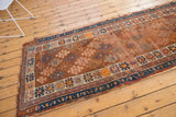 Antique Caucasian runner detail: copper and blue shrub motifs, geometric border, varied texture.