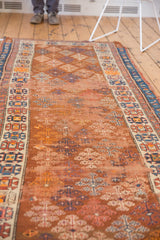 Antique Caucasian runner's copper guli hennai shrub motif, blue geometric border, and tattered side.
