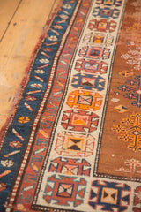 Geometric borders of an antique Caucasian rug runner with navy, ivory, copper tones, and worn fringe.
