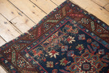 Vintage Heriz rug corner with navy floral field, wine red serrated border, and frayed edges.
