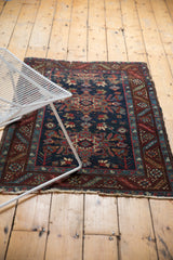 Vintage Heriz rug corner with navy, wine red serrated leaf vine border, and tattered ends.