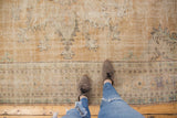 Distressed Oushak carpet showing worn pile, faded apricot, ivory, and subtle mint green patterns.
