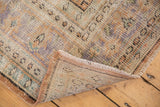 Distressed vintage Oushak rug with mostly even wear, folded edge, and pastel tones.