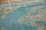 Textured distressed Oushak carpet with worn blue pile and faded ivory floral design.