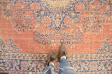 Distressed vintage Oushak carpet showcasing ornate blush and pale blue floral motifs.