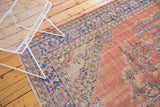 Distressed Oushak rug with ornate dusty blush and pale royal blue scrolling floral pattern.