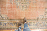 Distressed vintage Oushak carpet with abrashed pale rose field and faded blue corner pattern.