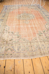 Distressed Oushak rug corner with fringe, abrashed rose field, and visible worn border.