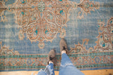 Distressed vintage Oushak rug with faded sky blue field, intricate apricot vinery, and visible pile wear.