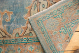 Distressed sky blue and apricot Oushak rug corner, showing worn pile, geometric border, and intact selvage.