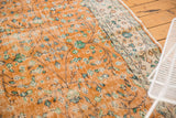 Distressed apricot orange Oushak rug with scrolling vinery, faint foundation showing, and ivory border.