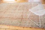 Distressed Oushak rug corner with faded apricot, ivory scrolling vinery, and even wear.