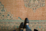 Distressed vintage Oushak carpet showing even wear, faded apricot field, and subtle blue patterns.
