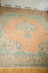 Distressed vintage Oushak rug corner with fringe, revealing worn peach and soft blue patterns.