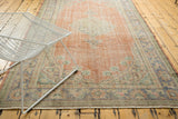 Distressed vintage Oushak rug showcasing faded red field and muted multicolor borders.