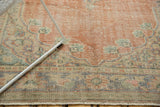 Distressed texture of vintage Oushak rug, showing faded red field and worn curvilinear motifs.